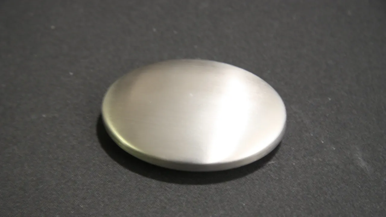 A round brushed metal disc on a dark work surface