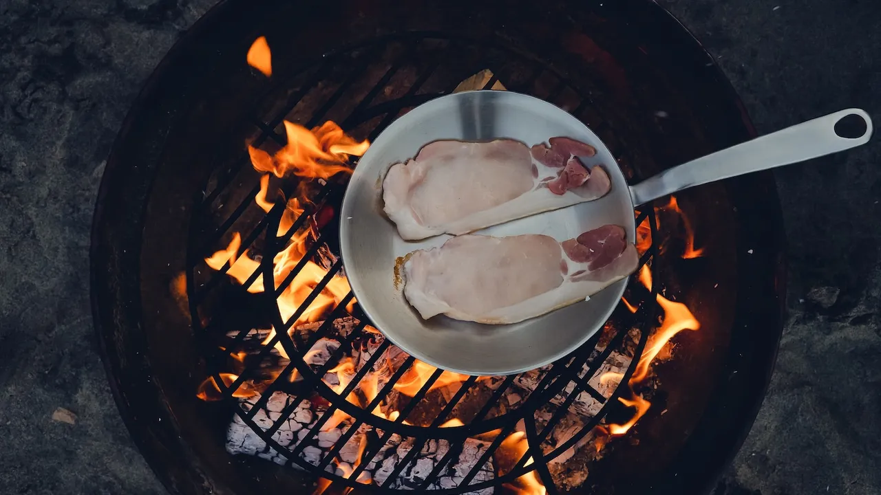 A stainless steel frying pan cooking over an open fire