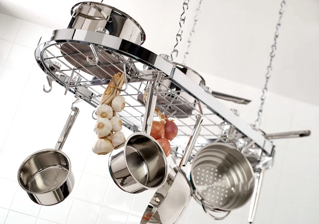 Polished stainless steel pots hanging from a kitchen rack