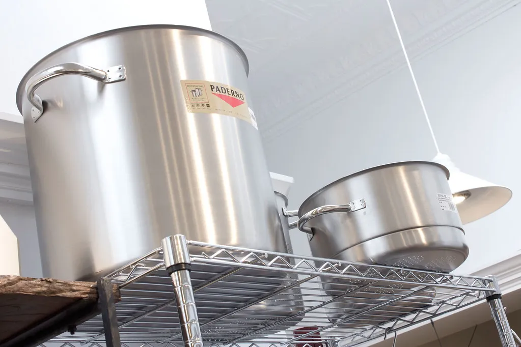 Large stainless steel stockpots displayed on wire shelving