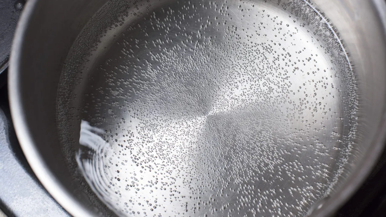 Small water beads forming across the inside of a heated stainless steel pan