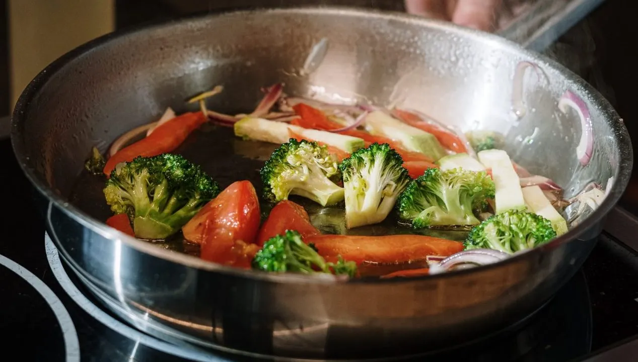 Broccoli, tomatoes, and other vegetables cooking in a stainless steel skillet