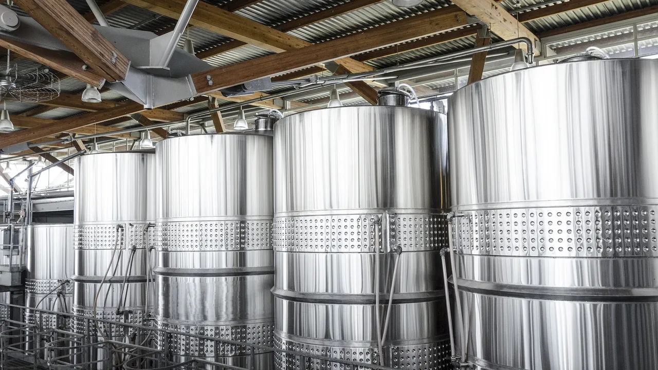 Wine bottle and glasses beside stainless steel winery tanks
