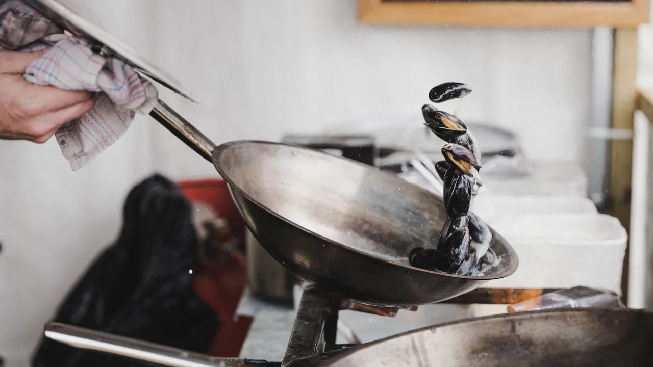 A cook tossing mussels in a stainless steel sauté pan